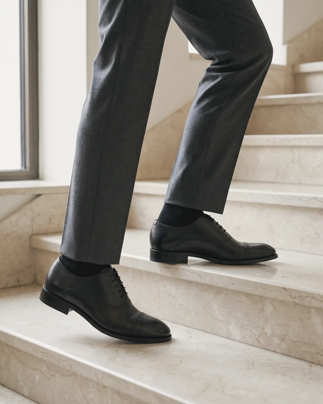 Black cap-toe oxfords with charcoal trousers on stone stairs