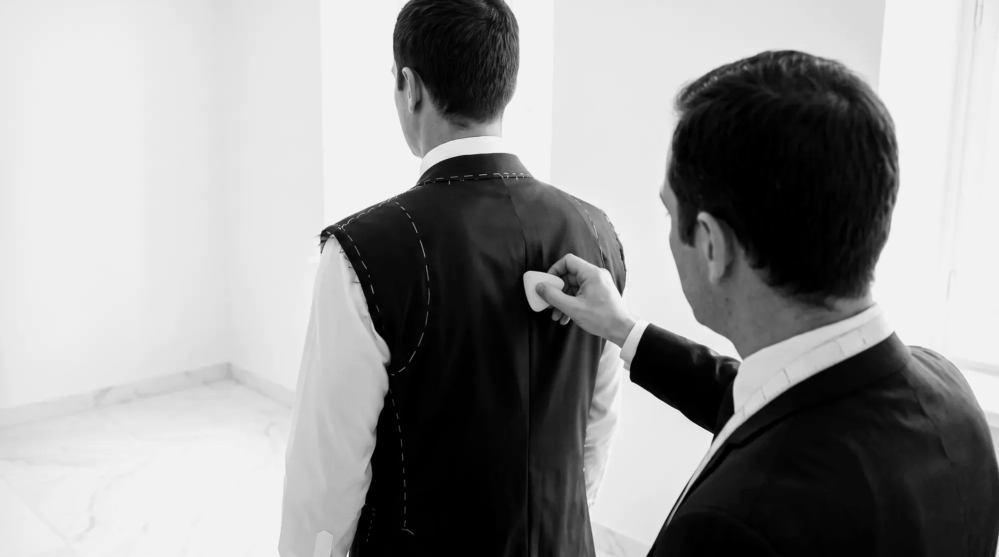 A tailor marking a jacket on a client from behind
